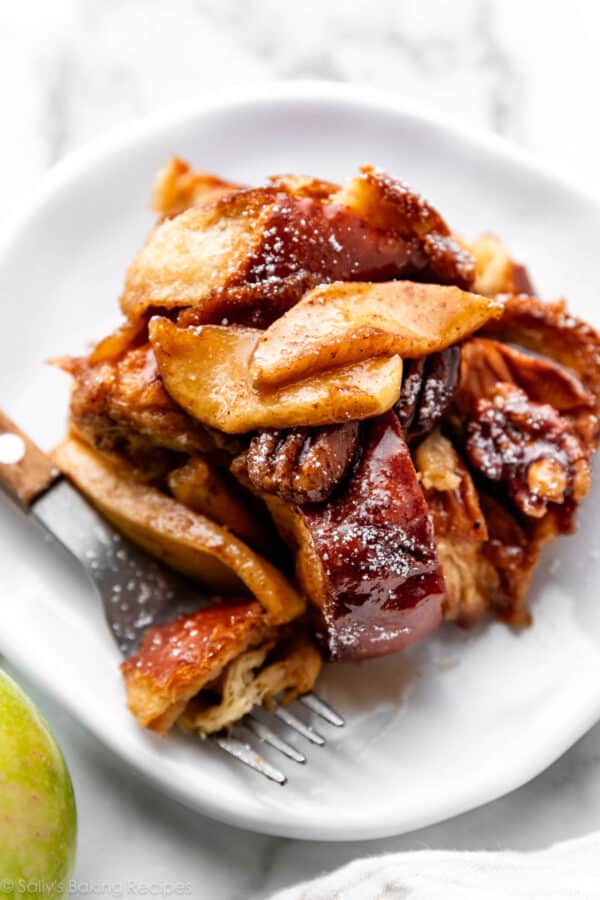 serving of baked apple cider french toast on white plate with apples and pecans on top.