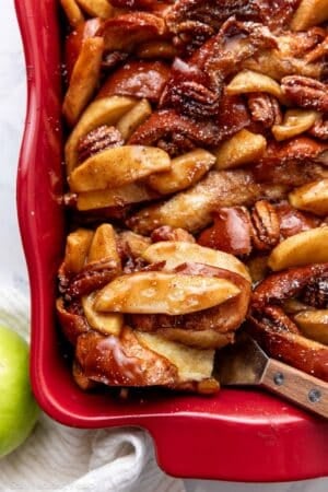 scooping serving of apple french toast out of red casserole dish.