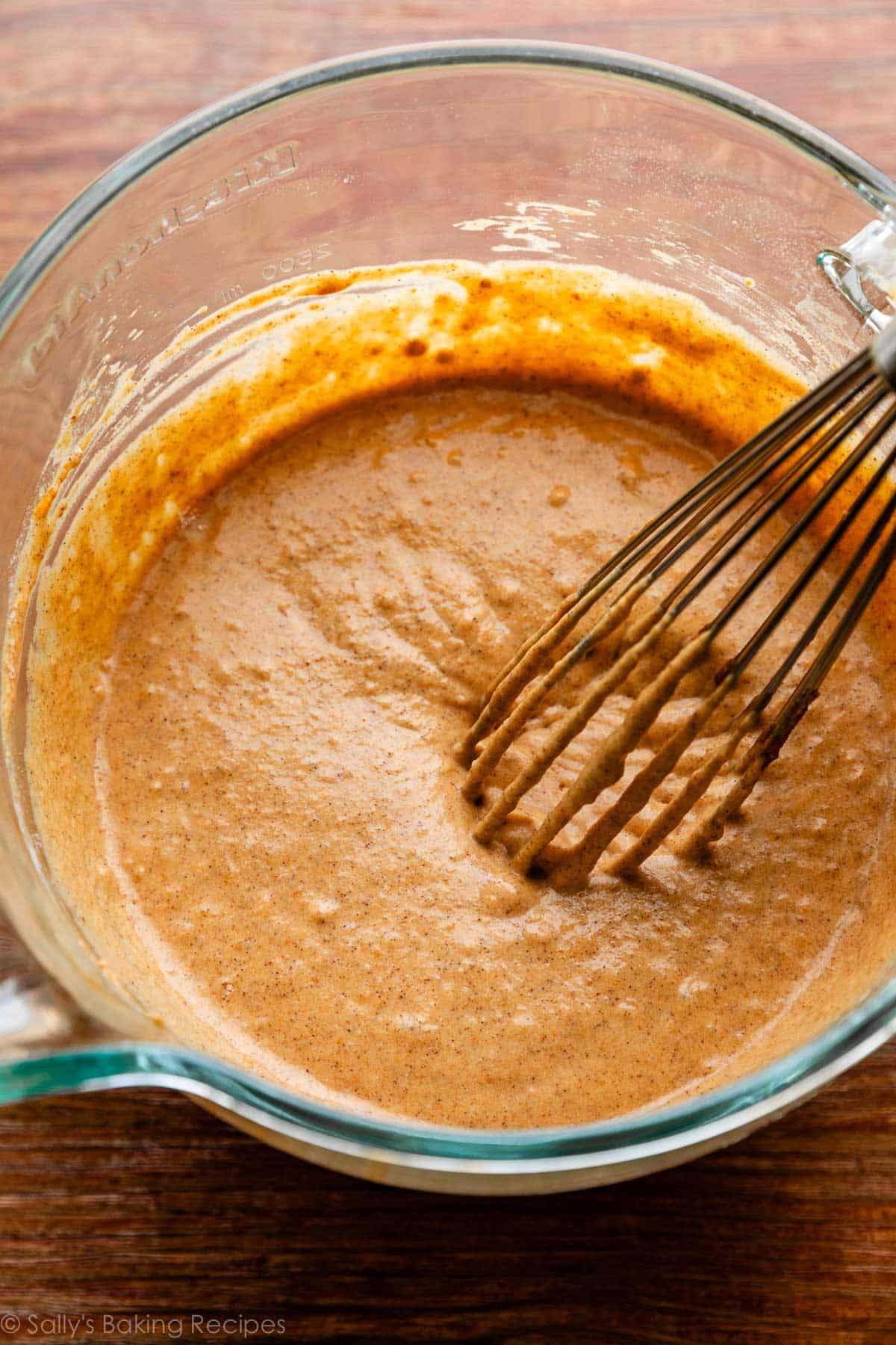 pumpkin batter in glass bowl with whisk on wooden surface.