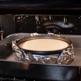 cheesecake batter in wrapped aluminum foil sitting in water bath in the oven.