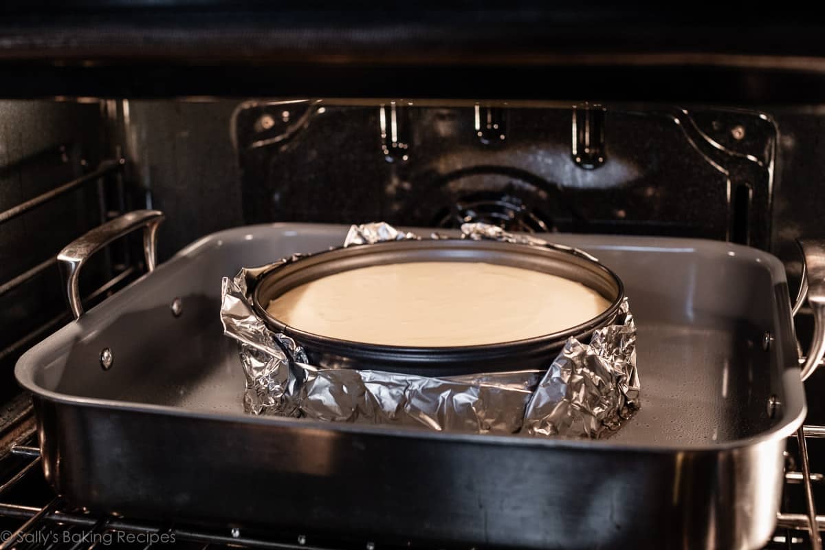 cheesecake batter in wrapped aluminum foil sitting in water bath in the oven.