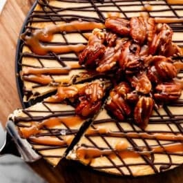 turtle cheesecake with caramel sauce, melted chocolate, and pile of caramel pecans on top with sea salt.