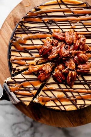 turtle cheesecake with caramel sauce, melted chocolate, and pile of caramel pecans on top with sea salt.