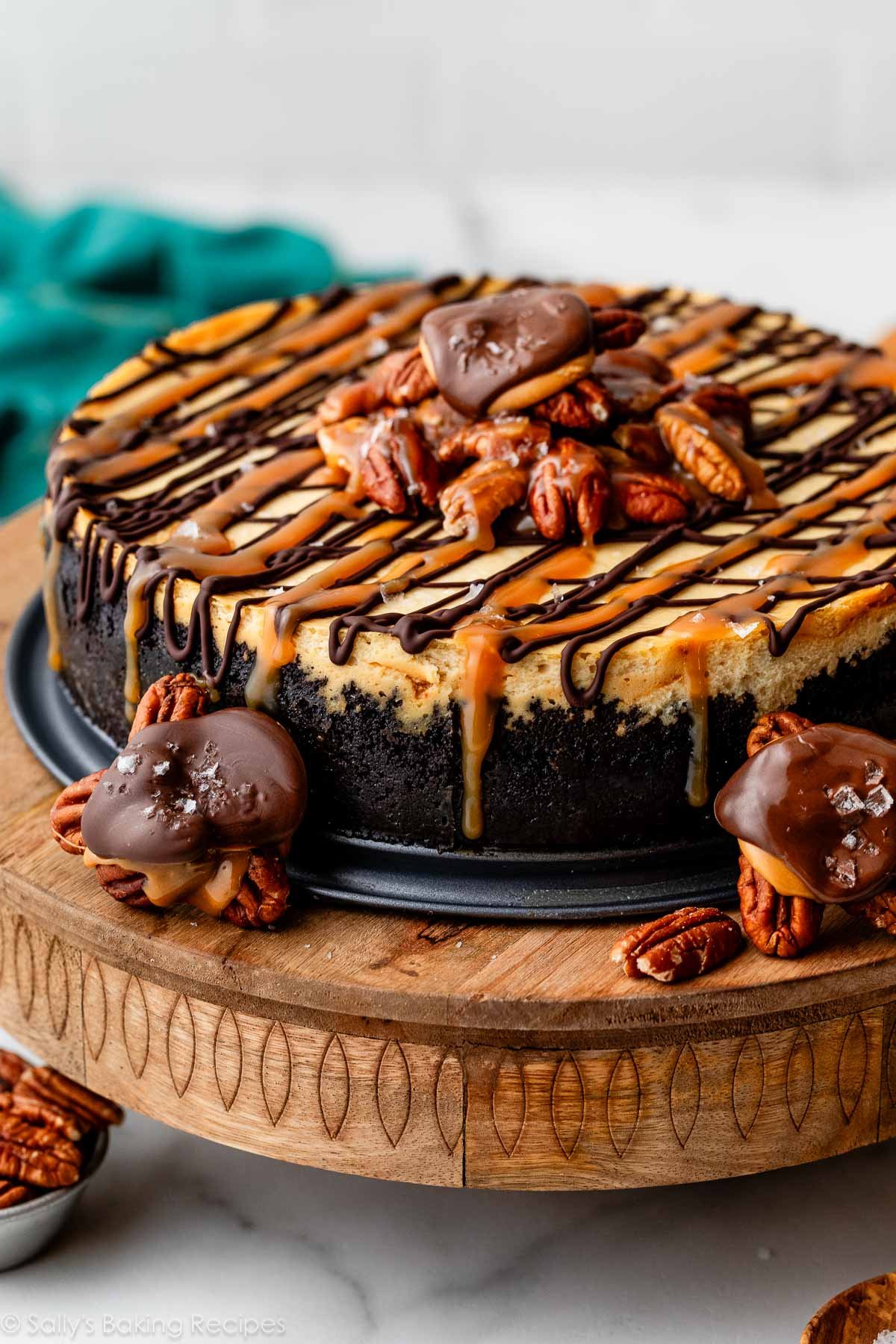 side view of caramel pecan turtle cheesecake with chocolate turtle candies around it.
