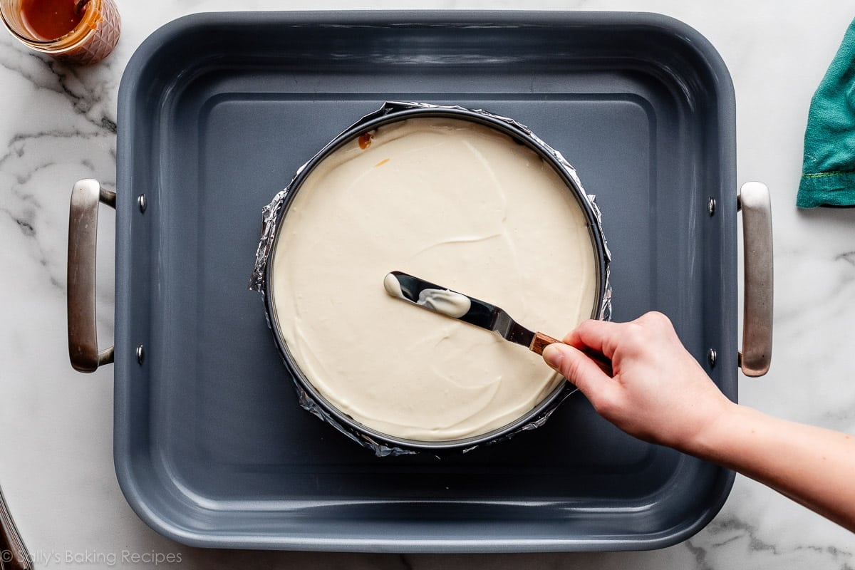 hand spreading batter with offset spatula in springform pan set in a roasting pan.