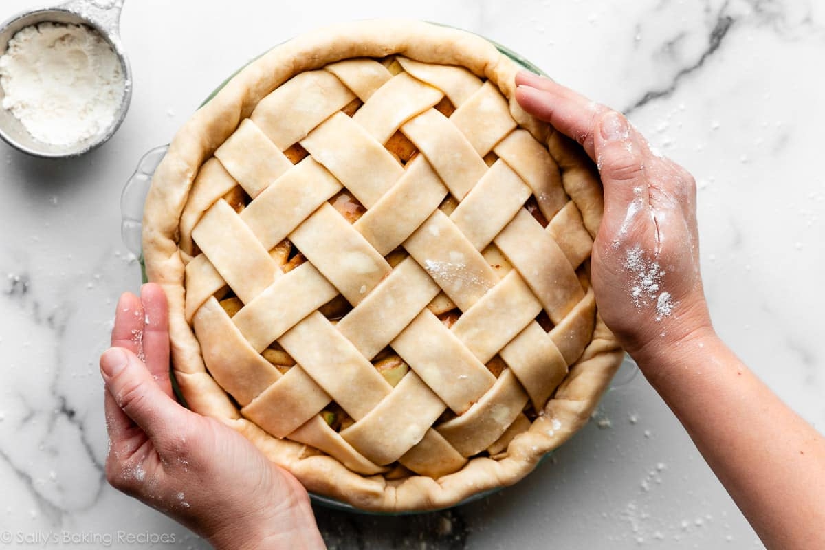 hands holding and tightening the edges of a lattice-designed pie crust.