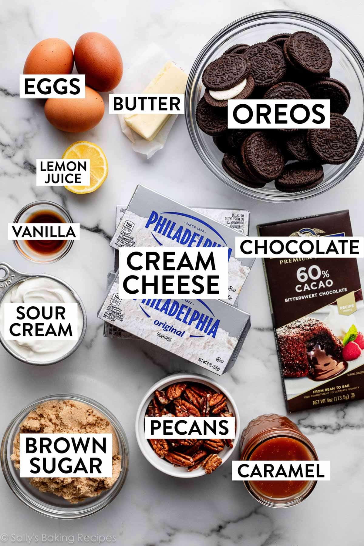 ingredients on counter including measured out Oreos in bowl, butter, eggs, half lemon, vanilla, sour cream, brown sugar, cream cheese blocks, and chocolate bar.