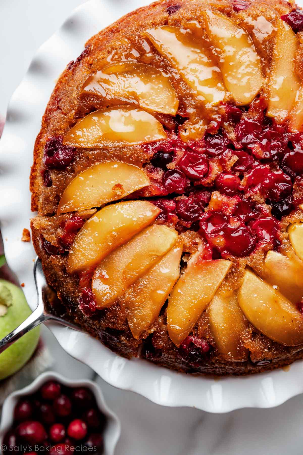 cranberry apple upside down fall cake on white cake stand with slice being removed.