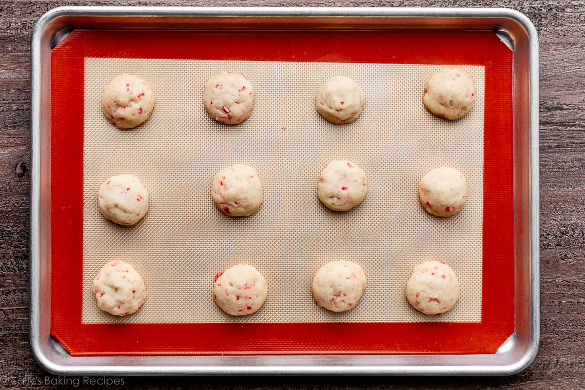 snowball candy cane cookies on lined baking sheet.