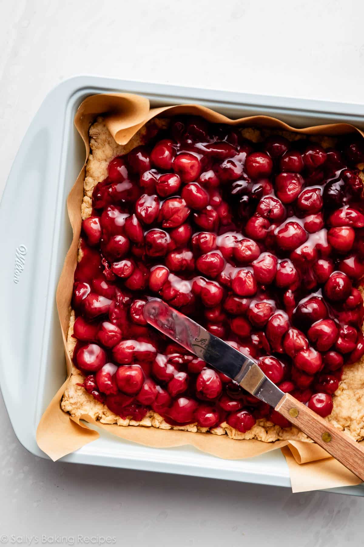 cherries being spread over a crust in a lined baking pan.