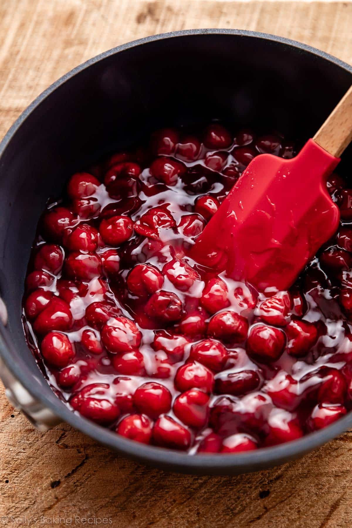 cherry pie filling in pot with red spatula.