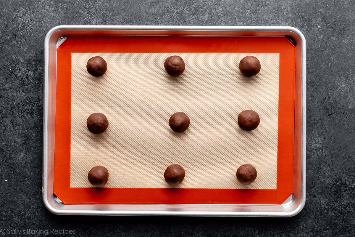 chocolate cookie dough balls on silicone baking mat-lined baking sheet.