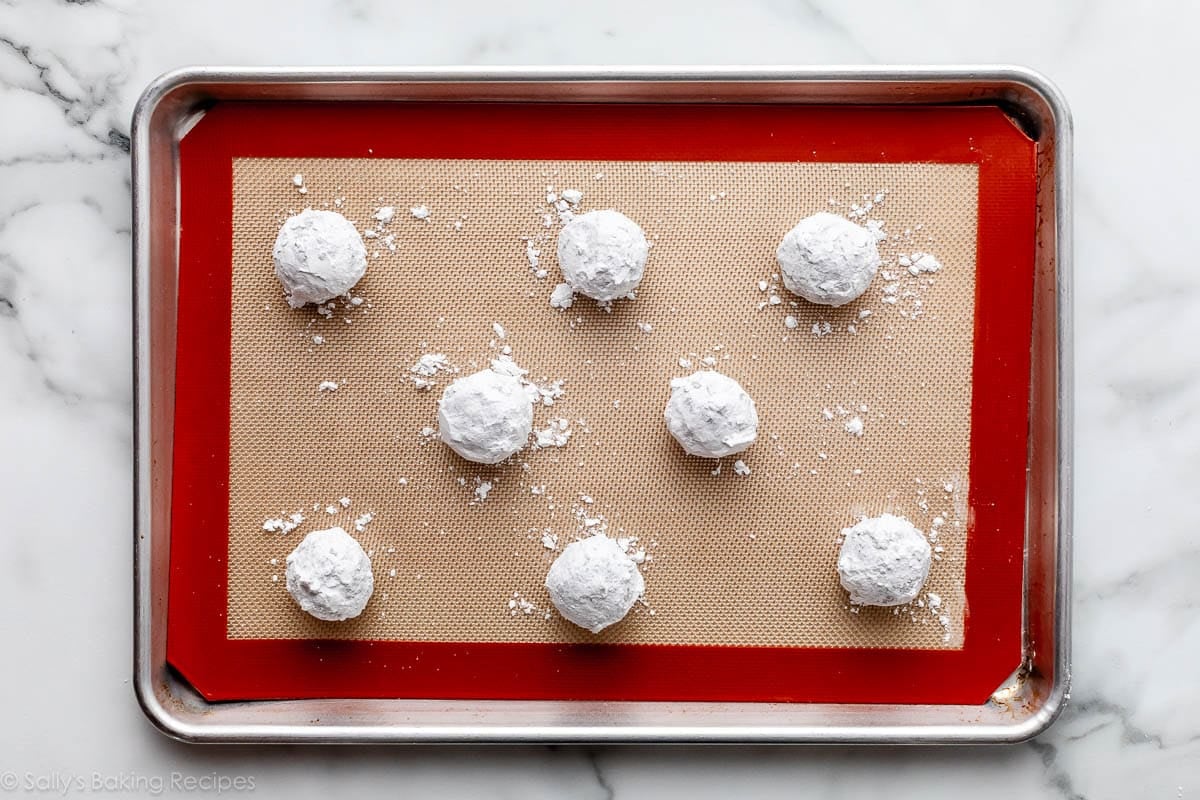 confectioners' sugar coated dough balls on silicone baking mat-lined baking sheet.