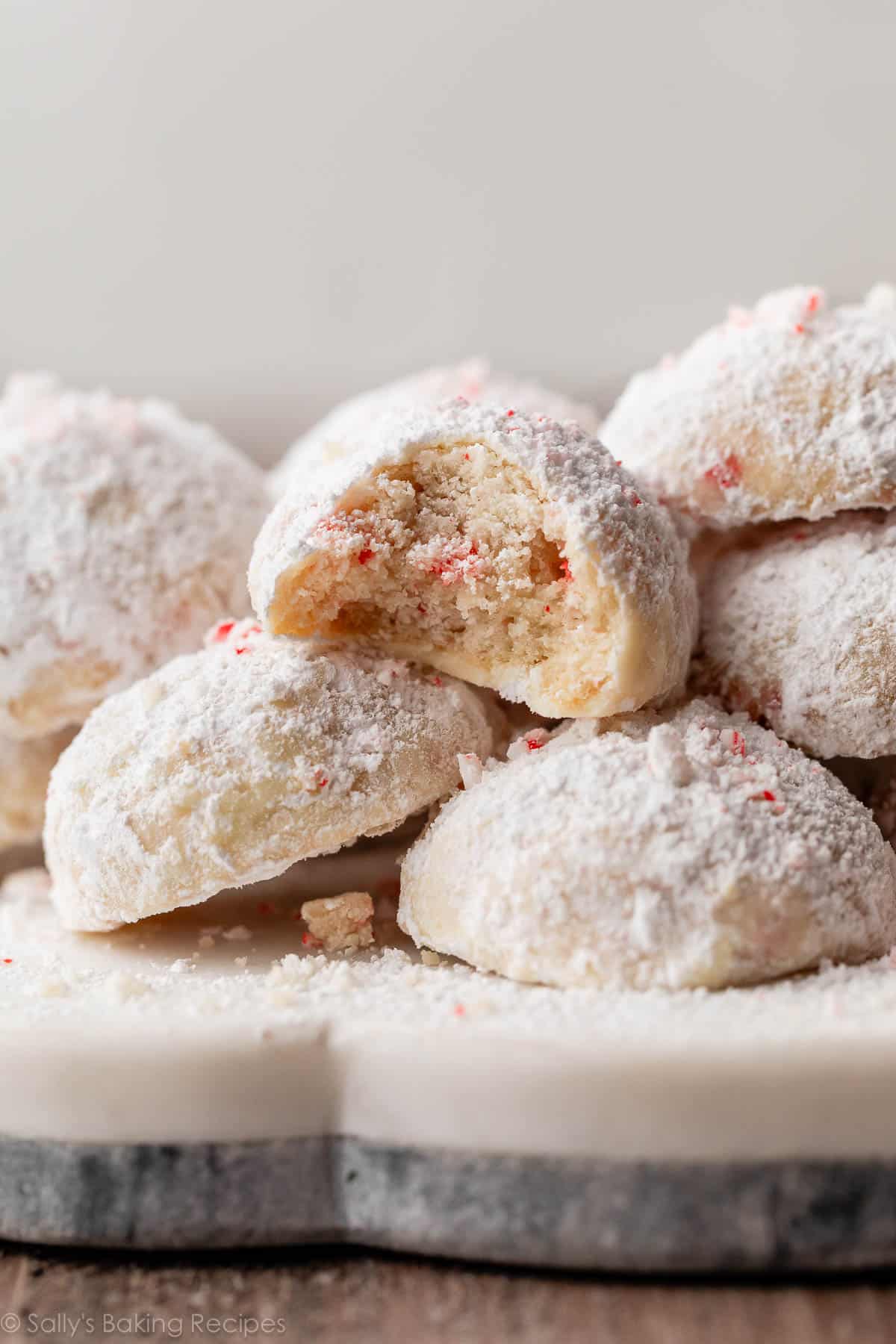 pile of candy cane snowball cookies covered in confectioners' sugar.