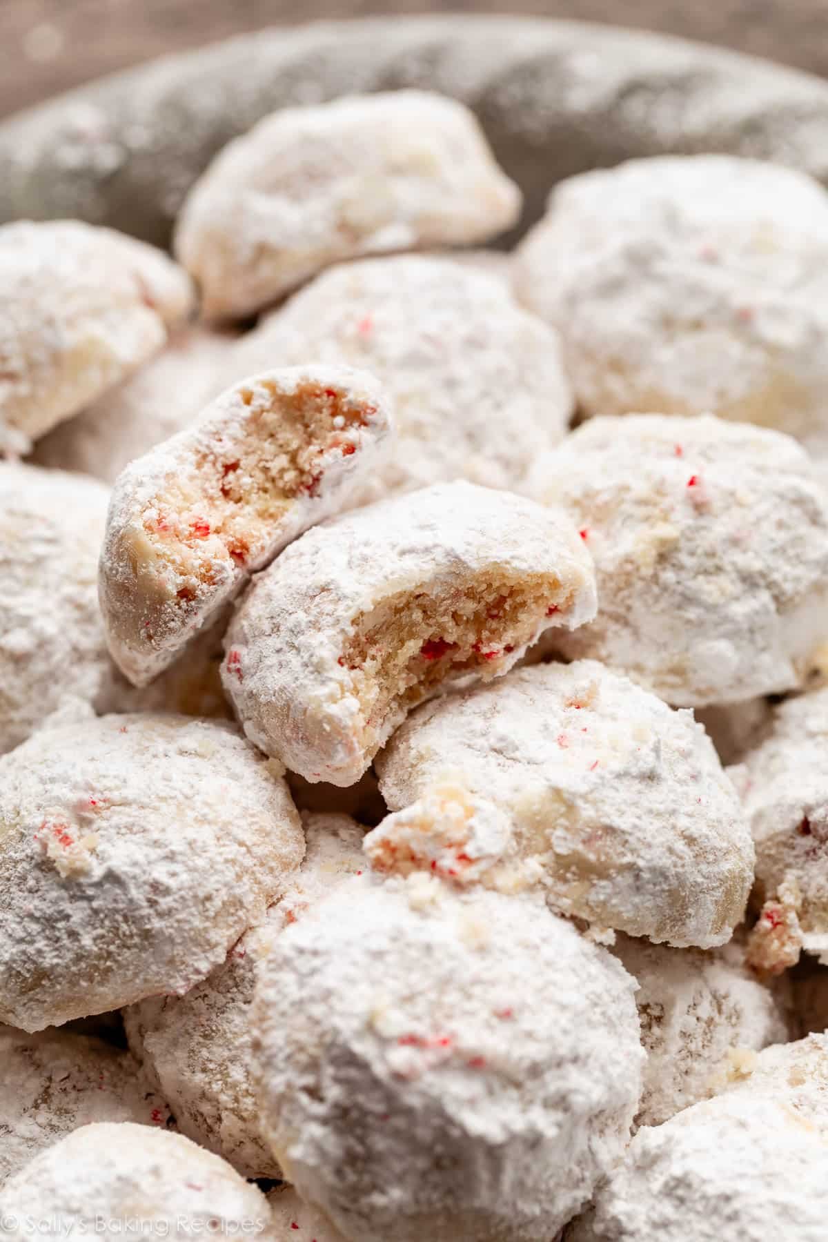 peppermint snowball cookies piled on top of one another with one with a bite taken out.