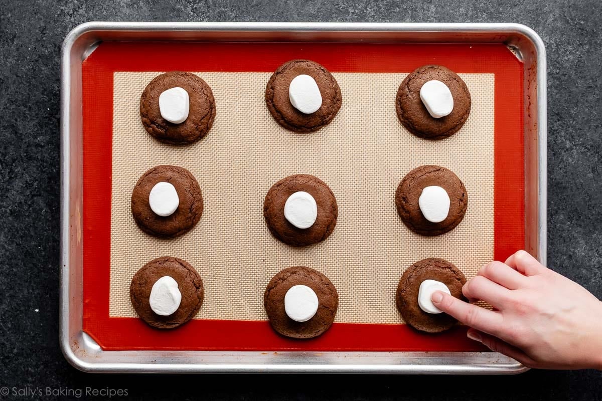 hand pressing marshmallow into tops of chocolate cookies on baking sheet.
