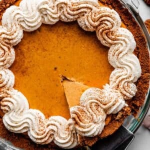 pumpkin cheesecake pie with whipped cream on top and slice being taken out.