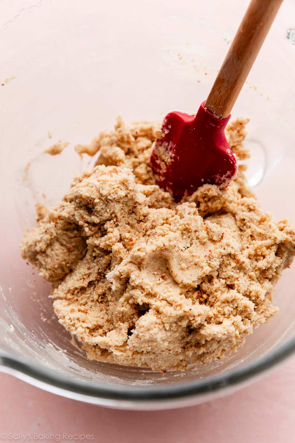 slow-up of almond linzer cookie dough in glass bowl with red spatula.