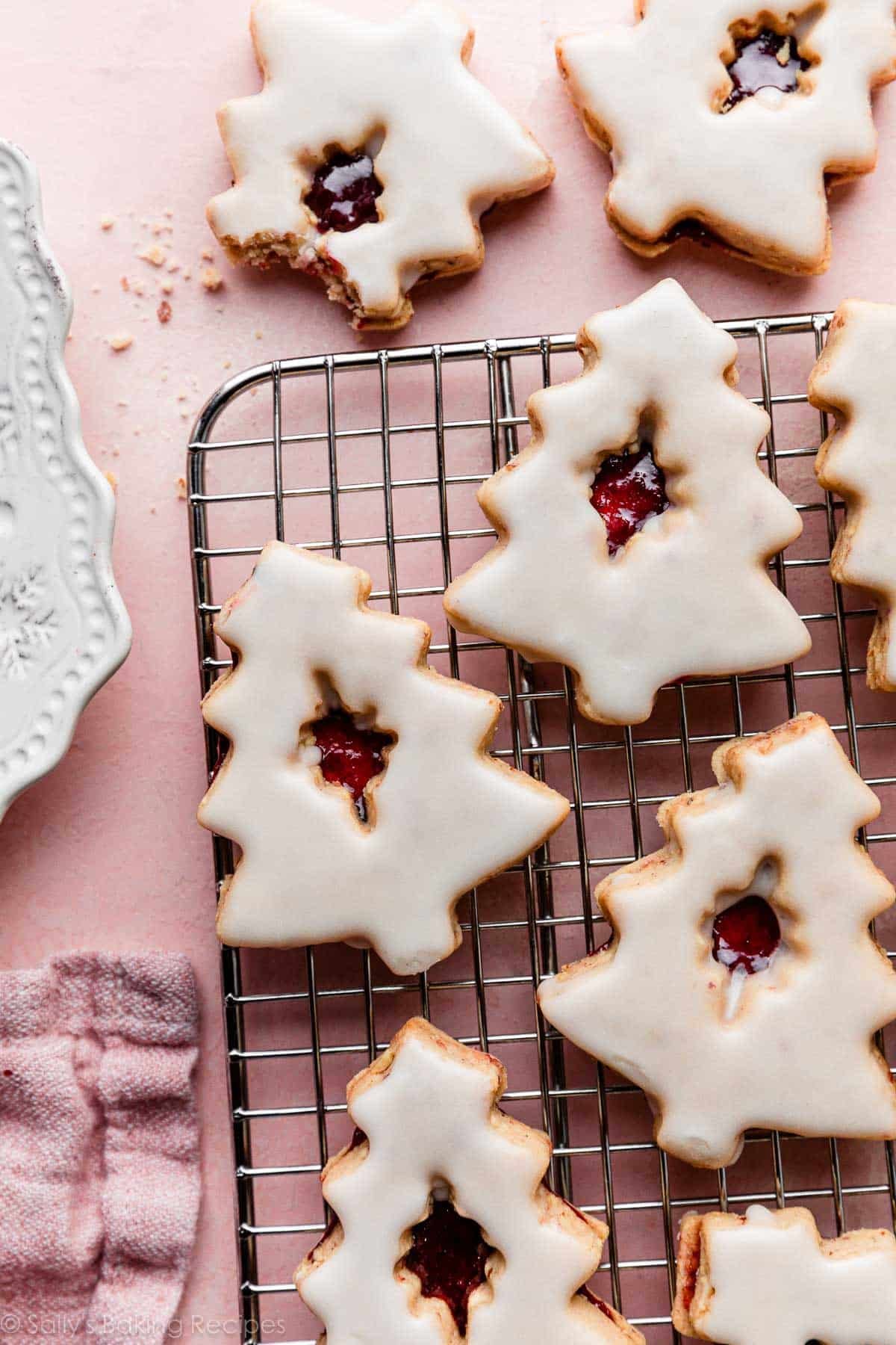 Christmas-tree shaped cherry almond linzer cookies with icing on cooling rack.