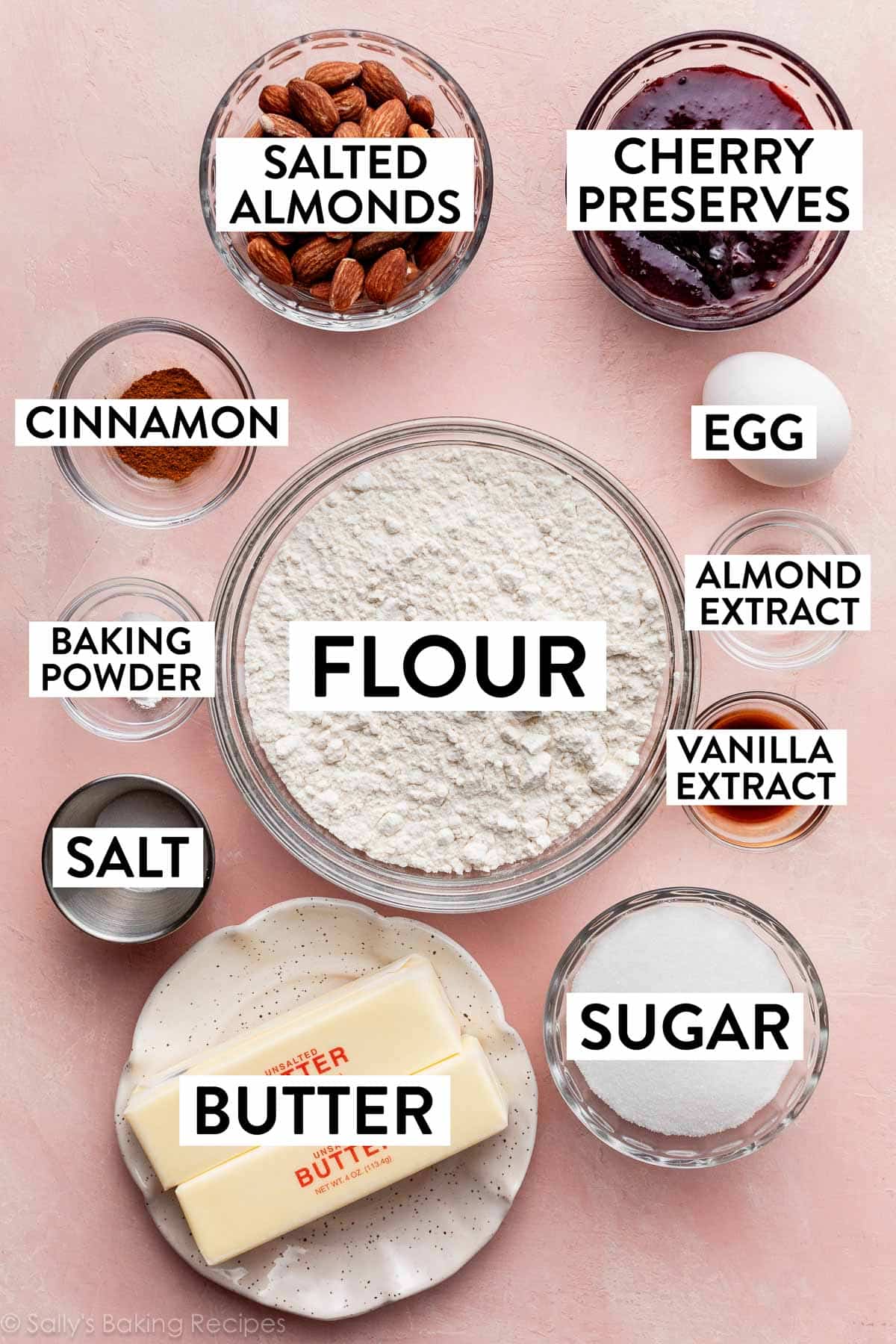 ingredients on pink backdrop including flour, jam, almonds, butter, sugar, egg, vanilla, and cinnamon.