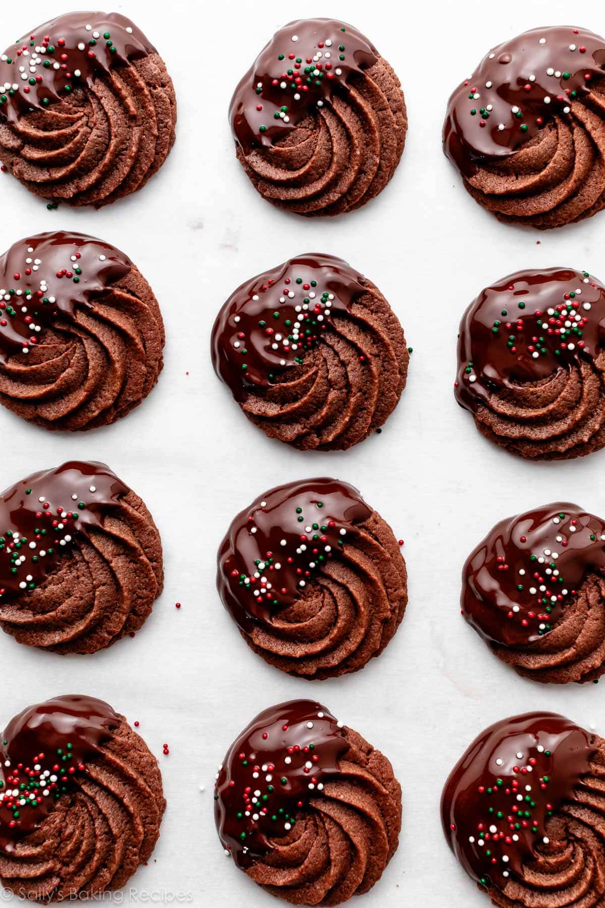 piped chocolate butter cookies dipped in chocolate with nonpareils on top.