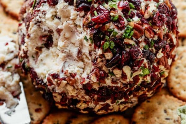 cranberry white cheddar cheese ball cut open with crackers on plate.