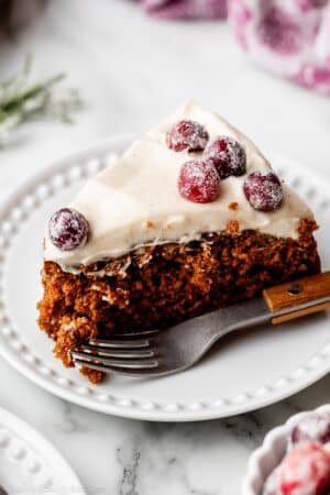slice of gingerbread cake with cream cheese frosting on top and sugared cranberries.