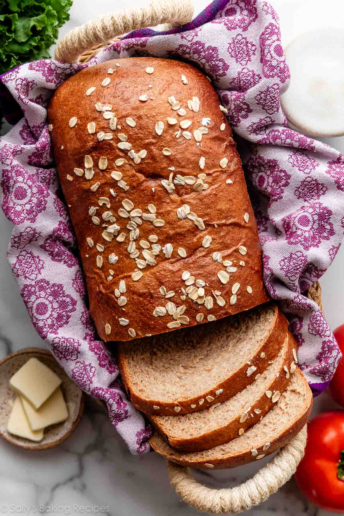 whole wheat loaf of bread with oats on top sitting in basket with purple linen.