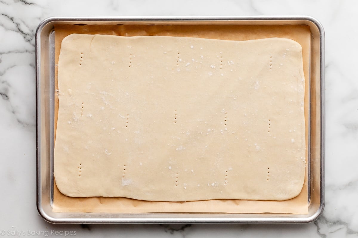 rolled-out dough with fork dock marks all over it on top of lined baking sheet.