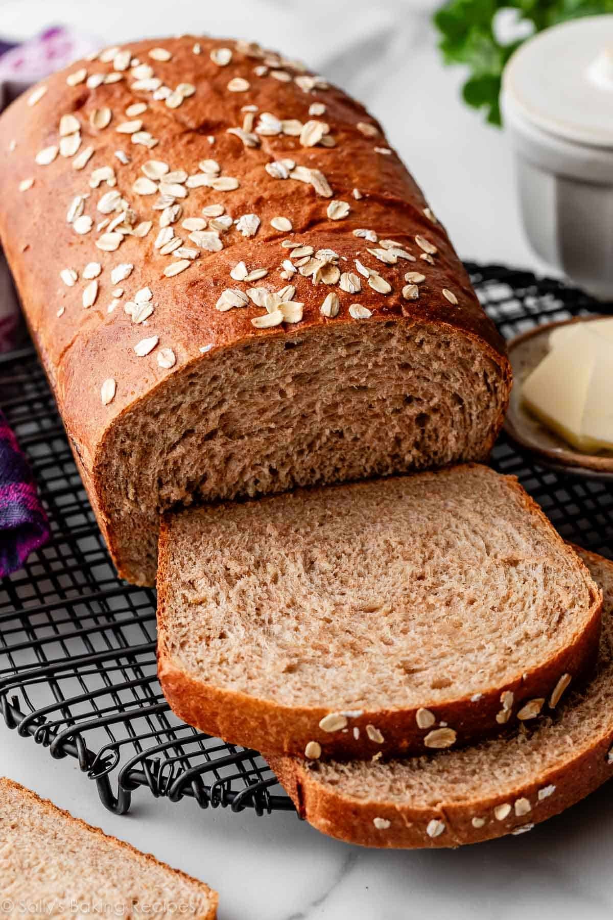 whole wheat bread loaf with two slices cut on black wire rack.