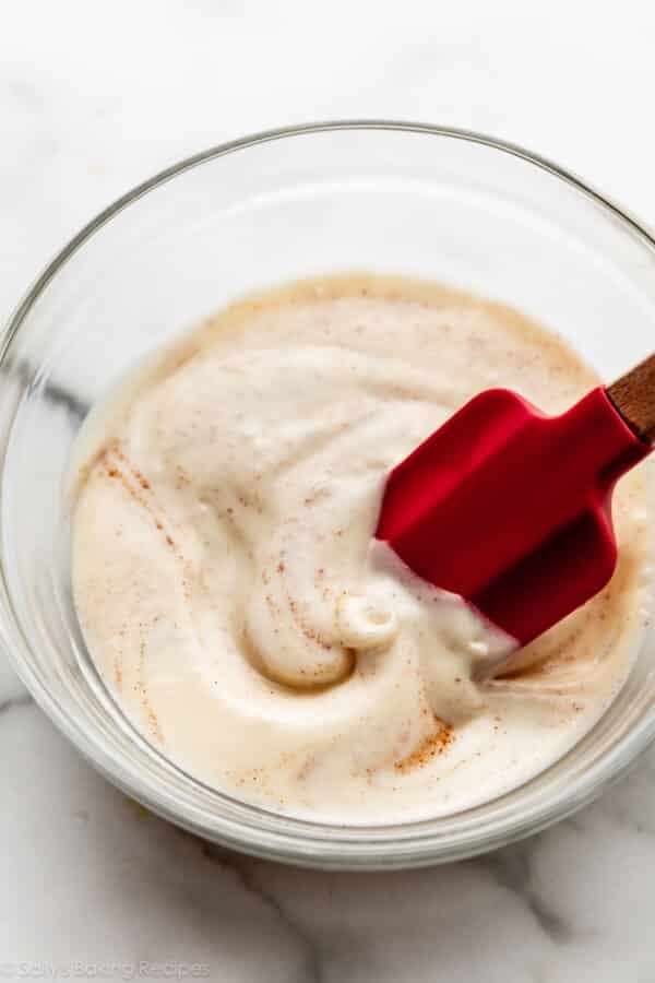 cream cheese icing with cinnamon in glass bowl with red spatula.