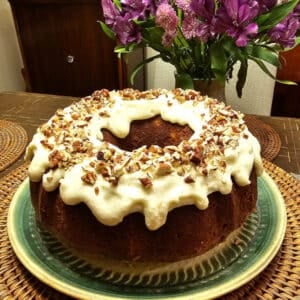 hummingbird bundt cake on plate with flowers in background.