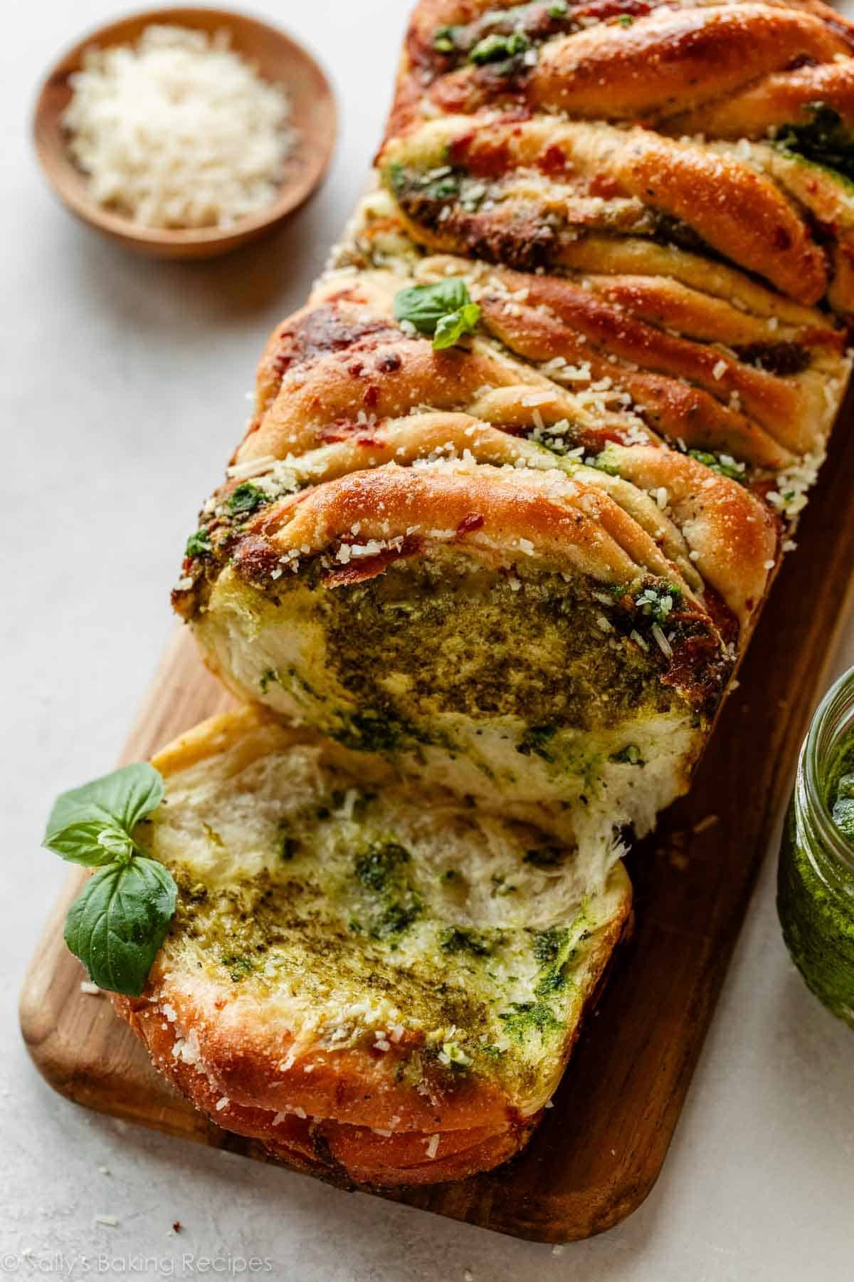 pesto bread with 1 piece torn off on wooden cutting board.