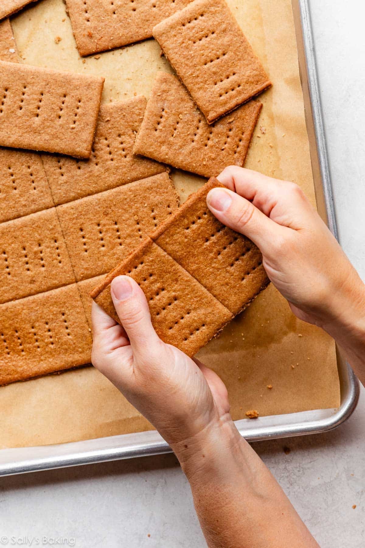 two hands breaking baked graham crackers apart along their seams.