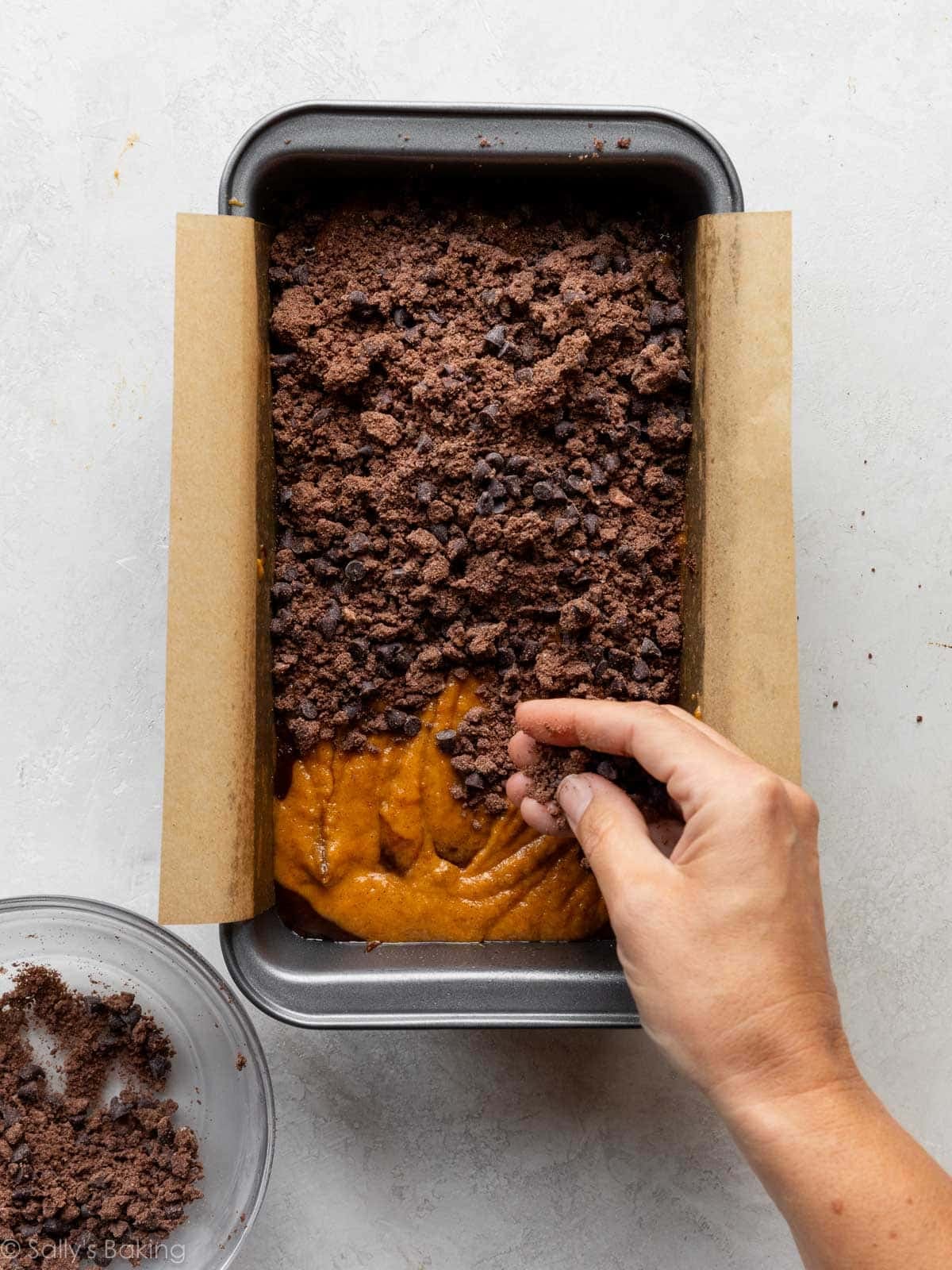 hand sprinkling chocolate streusel on top of batter in a loaf pan.