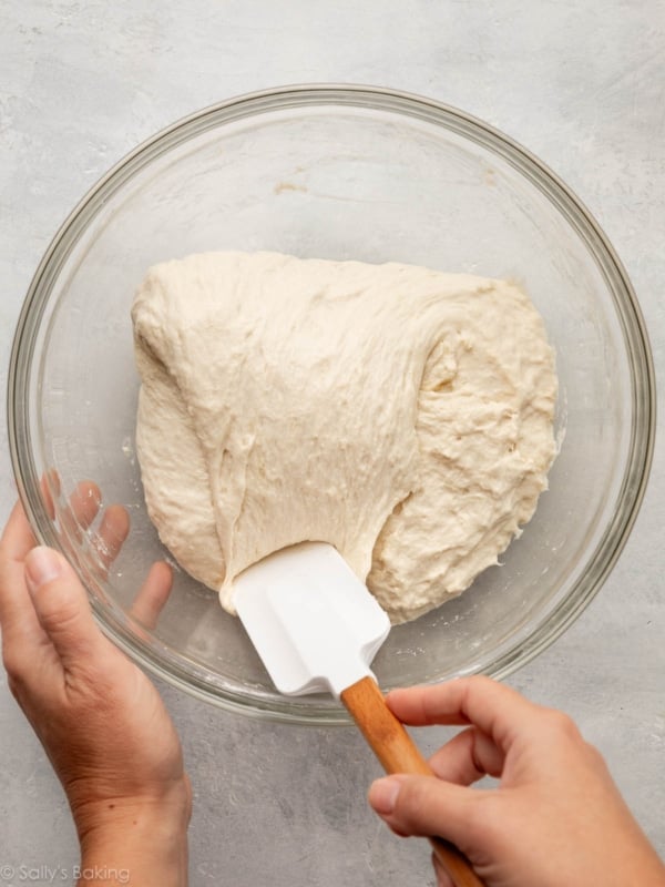 spatula folding focaccia dough in bowl.
