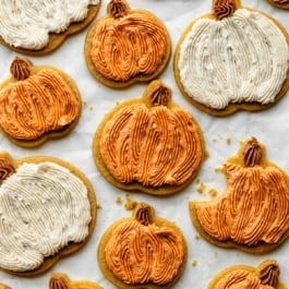 Frosted pumpkin sugar cookies on parchment paper.