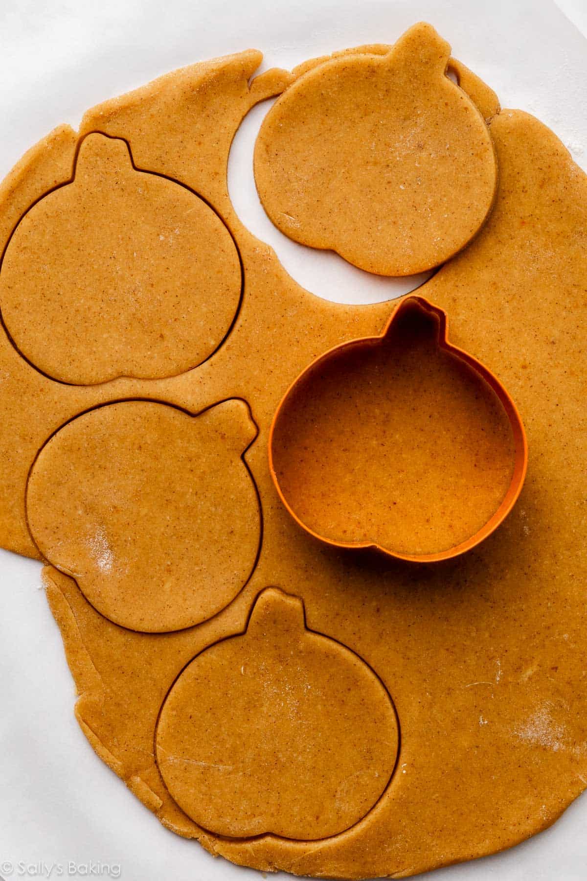 Cutting pumpkin sugar cookie dough with a pumpkin-shaped cookie cutter.