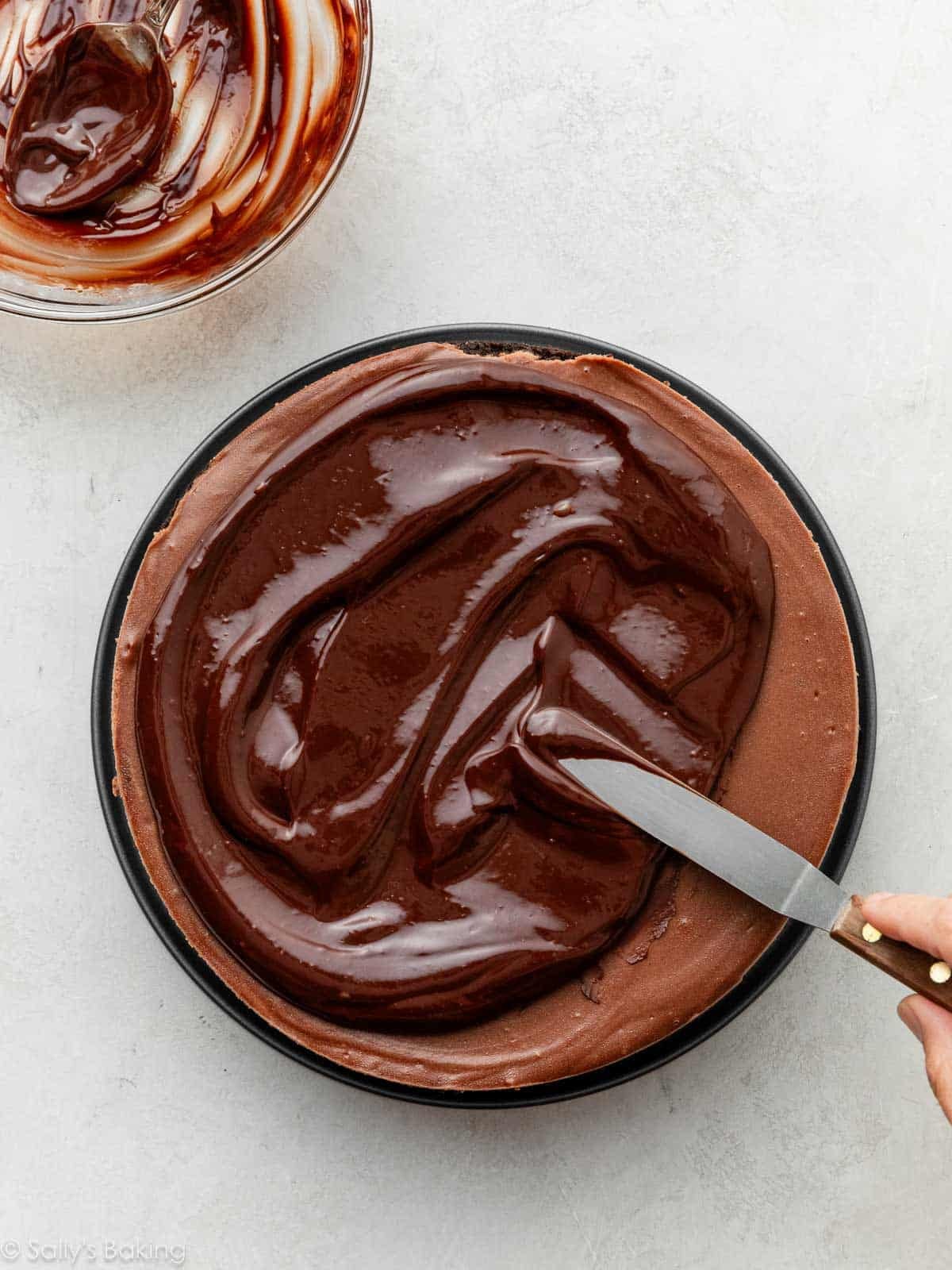 spreading chocolate ganache on top of chocolate cheesecake with an offset spatula.
